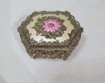 May include: A small, octagonal, silver-tone trinket box with an ornate design. The lid features a raised, pink flower with gold accents.
