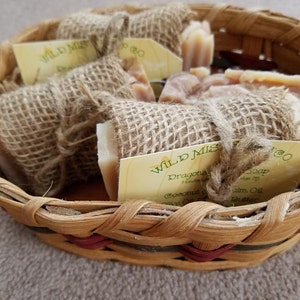 May include: A basket filled with handmade soap bars wrapped in burlap. The soap bars are labeled "Wild Mist Soap" and "Dragon's Blood". The soap is made with coconut oil, olive oil, palm oil, and shea butter.