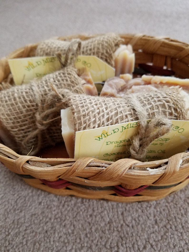 May include: A basket filled with handmade soap bars wrapped in burlap. The soap bars are labeled "Wild Mist Soap" and "Dragon's Blood". The soap is made with coconut oil, olive oil, palm oil, and shea butter.