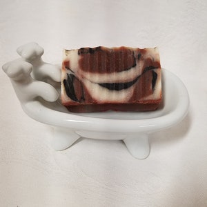 May include: A brown and white marbled soap bar in a white ceramic bathtub-shaped soap dish.