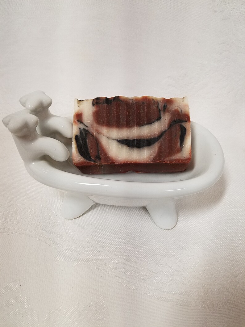 May include: A brown and white marbled soap bar in a white ceramic bathtub-shaped soap dish.