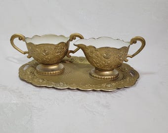 Juego antiguo de cremera y azucarero dorados ornamentados sobre una bandeja a juego.