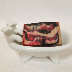 May include: A red, black, and white marbled soap bar in a white ceramic bathtub-shaped soap dish.