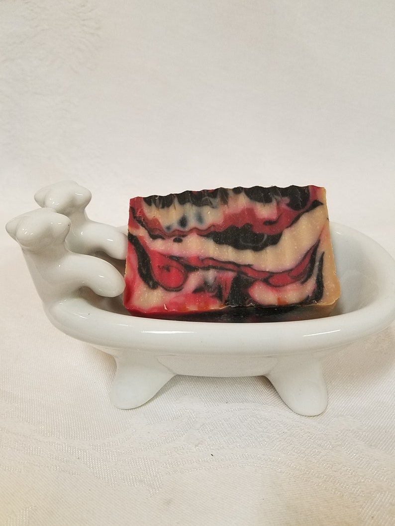 May include: A red, black, and white marbled soap bar in a white ceramic bathtub-shaped soap dish.