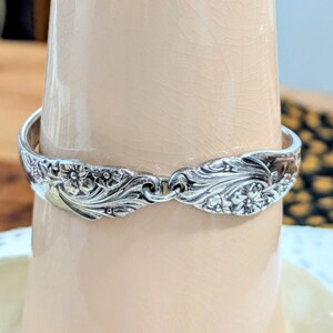 May include: A silver spoon bracelet with a floral design. The bracelet is made from a vintage spoon and is a unique piece of jewelry.