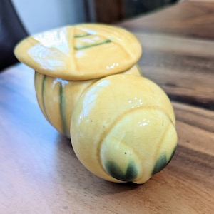 May include: A ceramic bee-shaped honey pot with a lid. The pot is yellow with green accents and a glossy finish.