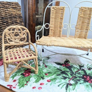 May include: A miniature wicker chair with a woven back and seat, next to a small white metal and wicker bench. The chair has a decorative knot design on the back. The bench has a curved metal frame. The items are on a festive tablecloth.