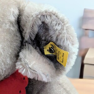 Pode incluir: Close-up de um animal de pel&uacute;cia cinza com uma etiqueta amarela que diz "Made in Germany - Preis = Price".