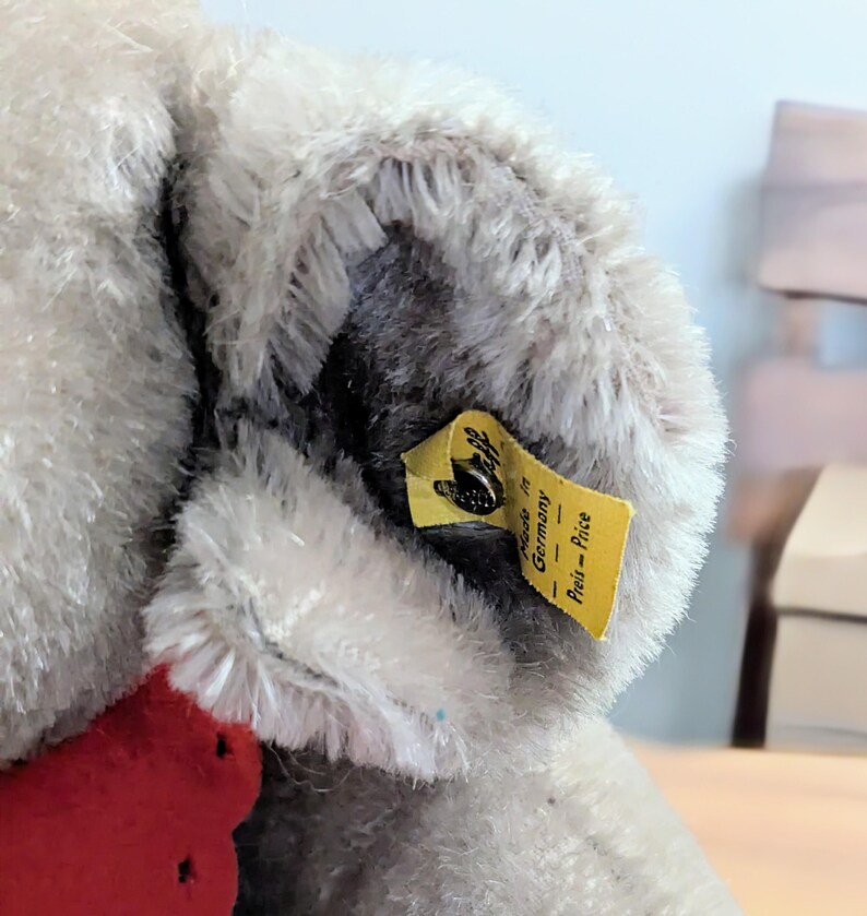 Pode incluir: Close-up de um animal de pel&uacute;cia cinza com uma etiqueta amarela que diz "Made in Germany - Preis = Price".