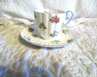 May include: A white teacup and saucer with a blue trim and floral pattern. The flowers are pink, blue, and yellow.