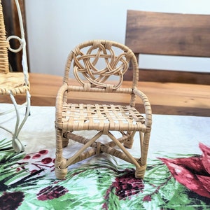 May include: A small, intricately woven wicker chair with a Celtic knot design on the backrest. The chair features a woven seat and is made of light brown wicker. It is placed on a festive floral patterned tablecloth.