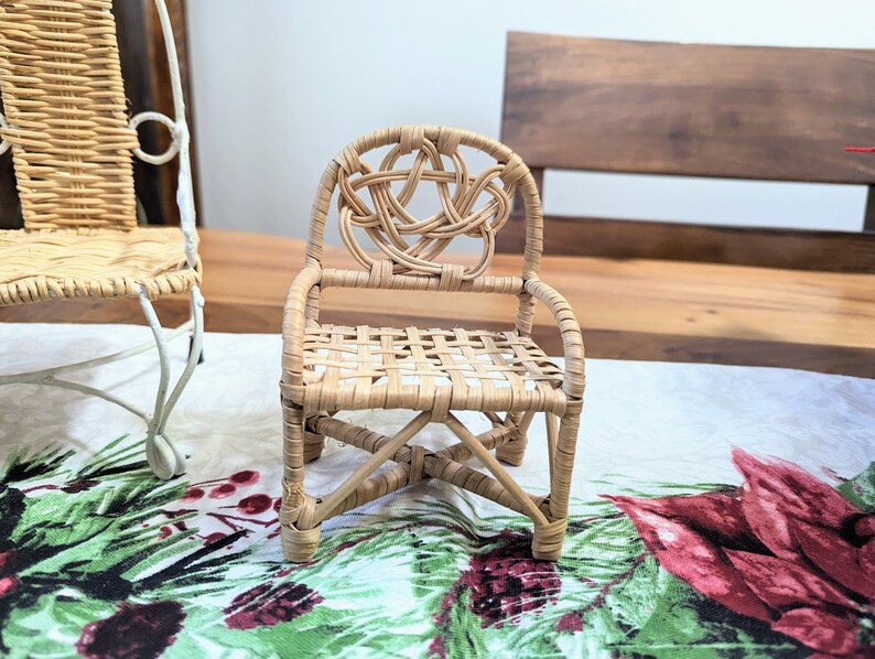 May include: A small, intricately woven wicker chair with a Celtic knot design on the backrest. The chair features a woven seat and is made of light brown wicker. It is placed on a festive floral patterned tablecloth.
