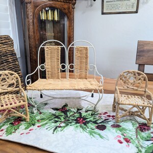 May include: Three miniature wicker chairs. A double seat bench with a white metal frame and woven back and seat. Two single chairs with woven seats and backs. The chairs are on a table runner with a Christmas theme.