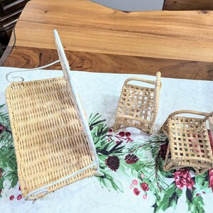 May include: Three miniature woven wicker chairs and a wall-mounted basket. The chairs are light brown with woven seats and backs. The wall basket has a white metal frame. The items are on a Christmas-themed tablecloth.