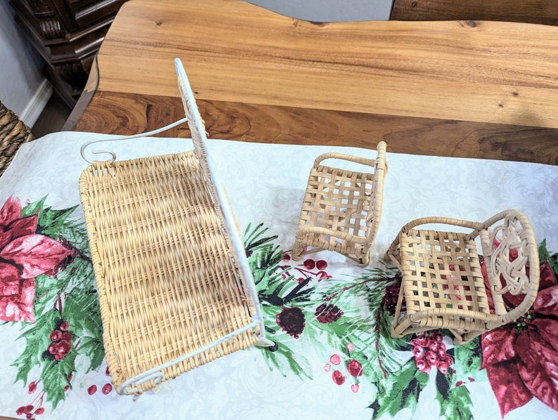 May include: Three miniature woven wicker chairs and a wall-mounted basket. The chairs are light brown with woven seats and backs. The wall basket has a white metal frame. The items are on a Christmas-themed tablecloth.