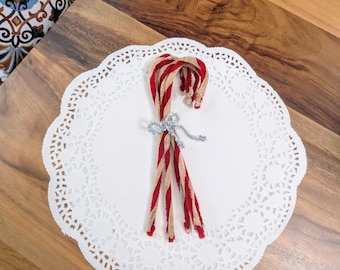 May include: Five red and white striped candy canes tied together with a silver sparkly ribbon on a white doily.