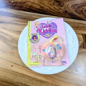 May include: A vintage Liddle Kiddles Becky Birthday Party doll in its original packaging. The packaging is pink and features a heart-shaped locket with a small doll inside. The packaging also includes the text "Ready For Fun Wherever You Go!"