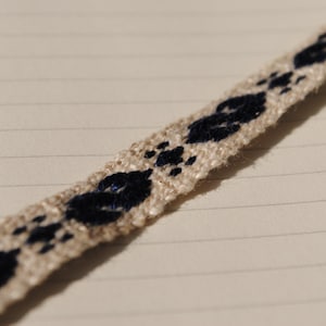 Peut inclure: Gros plan d'une garniture en tissu blanc avec un motif répétitif de formes géométriques bleu foncé. La garniture est tissée avec une texture subtile.