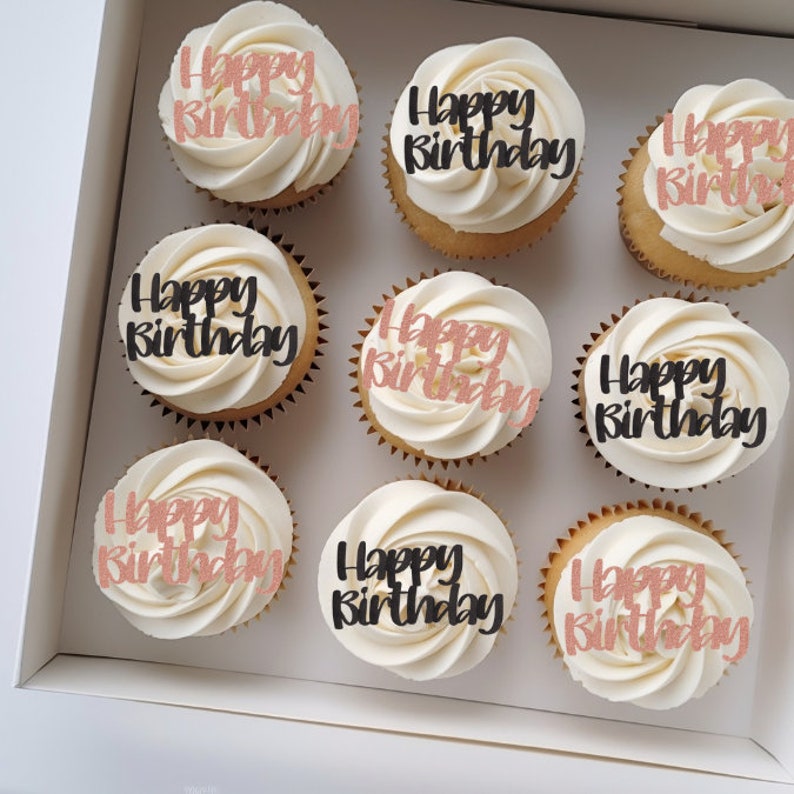 May include: Nine white cupcakes with vanilla frosting and black and rose gold glitter "Happy Birthday" toppers in a white box.