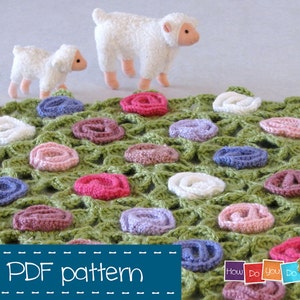 Puede incluir: Un patr&oacute;n de ganchillo para una manta verde con flores de ganchillo de colores. El patr&oacute;n se llama "How Do You Do It?" y est&aacute; disponible para descargar en PDF. Hay dos ovejas de juguete blancas en el fondo.