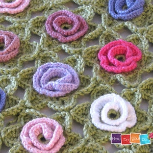 Puede incluir: Una manta de ganchillo con fondo verde y flores multicolores. Las flores est&aacute;n hechas de hilo y son de tonos rosa, morado, blanco y azul.