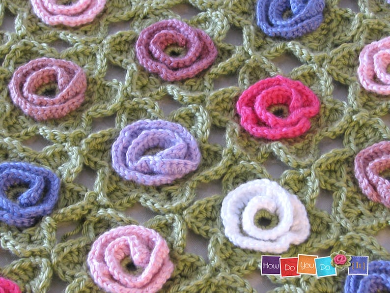 Puede incluir: Una manta de ganchillo con fondo verde y flores multicolores. Las flores est&aacute;n hechas de hilo y son de tonos rosa, morado, blanco y azul.