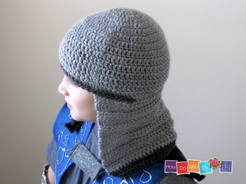 May include: A gray crocheted hat with a long flap that covers the neck and ears. The hat is made with a simple stitch pattern and has a black trim around the edge.