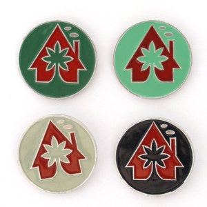 May include: Four round pins with a house design. Each pin has a different colored background: green, light green, black, and white. The house is red with a green leaf design on the roof.