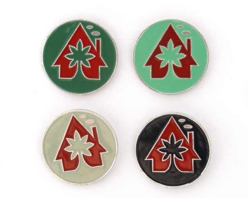 May include: Four round pins with a house design. Each pin has a different colored background: green, light green, black, and white. The house is red with a green leaf design on the roof.