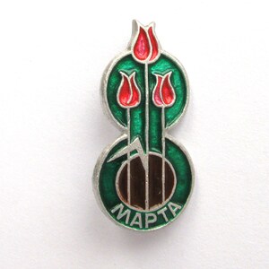 May include: A silver-toned metal pin featuring three red tulip flowers with green stems and leaves set against a circular green enamel background. The bottom of the pin displays the Cyrillic text MAPTA in silver lettering on a green enamel base.
