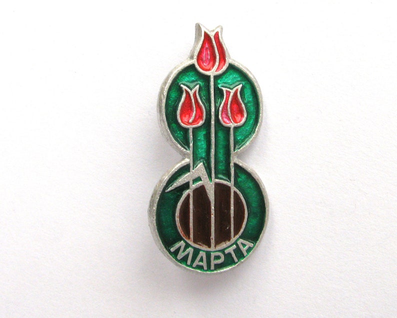 May include: A silver-toned metal pin featuring three red tulip flowers with green stems and leaves set against a circular green enamel background. The bottom of the pin displays the Cyrillic text MAPTA in silver lettering on a green enamel base.