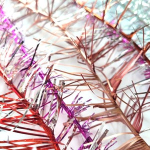 Puede incluir: Primer plano de oropel festivo en tonos rojo, plateado y oro rosa. El oropel está dispuesto en un patrón en capas, creando un efecto brillante y texturizado. Ideal para decoraciones navideñas.