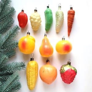 Puede incluir: Adornos navideños vintage con forma de frutas y verduras. Los adornos incluyen un pimiento rojo, coliflor, pimiento verde, pepino, zanahoria, manzana, pera, maíz, naranja y fresa.