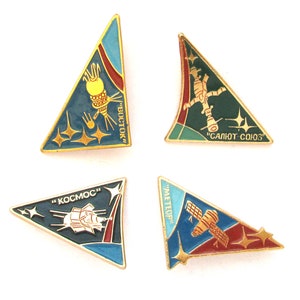 Puede incluir: Cuatro pines de esmalte triangulares con ribete dorado, cada uno representando una nave espacial soviética diferente. Los pines llevan los nombres "VOSTOK", "SALYUT-SOYUZ", "KOSMOS" y "METEOR" en escritura cirílica.