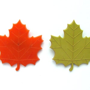 Op de afbeelding: Twee plastic esdoornbladeren, een oranje en een groen, op een witte achtergrond.