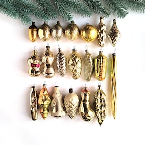 May include: A collection of 20 vintage glass Christmas ornaments in gold and green. The ornaments are shaped like acorns, pinecones, bells, and other festive shapes.