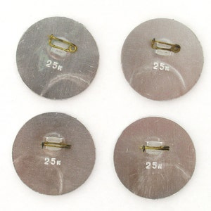 May include: Four silver-colored round pins with a safety pin closure. Each pin has the text "25k" printed on it.