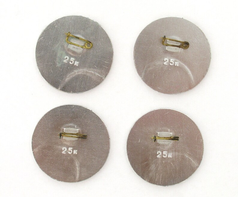 May include: Four silver-colored round pins with a safety pin closure. Each pin has the text "25k" printed on it.