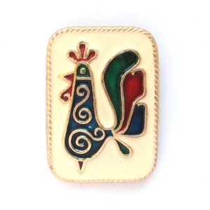Puede incluir: Un pin de esmalte dorado con un gallo estilizado con detalles en azul, verde y rojo. El gallo está representado en un estilo de arte popular tradicional con patrones en espiral.