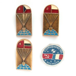 May include: Four vintage enamel pins featuring a hot air balloon with a flag and a globe. The flags are the Czech Republic, Bulgaria, and the Soviet Union. The fourth pin is a round pin with the text "СОТРУДНИЧЕСТВО В КОСМОСЕ" and the flags of the Soviet Union and France.