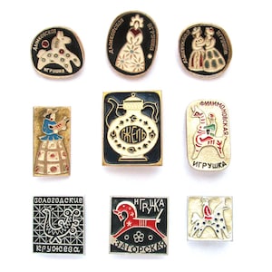 Puede incluir: Una colección de nueve broches de esmalte vintage con diseños de arte popular ruso. Los broches presentan varias formas y representan figuras, animales y patrones decorativos en una gama de colores que incluyen negro, rojo, blanco y dorado. Algunos broches incluyen texto cirílico.