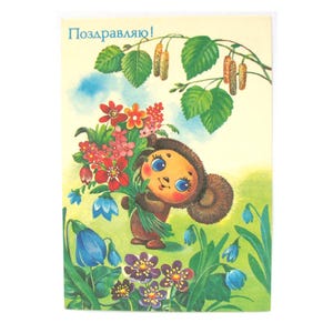 Può includere: Cartolina vintage con un personaggio dei cartoni animati che tiene un mazzo di fiori. Il personaggio è marrone con grandi occhi blu. Lo sfondo mostra fiori, erba e un ramo di betulla con foglie. Il testo "Поздравляю!" è in alto.