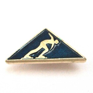 May include: A vintage pin in the shape of a triangle, featuring a gold-colored border. The pin has a dark blue enamel background with a gold-colored figure of a speed skater. A collectible sports-themed accessory.