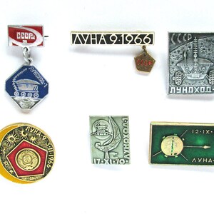 May include: A collection of six vintage Soviet space program pins. The pins feature the text "Luna 9", "Luna 2", "Lunokhod-1", and "USSR" along with images of the moon, a spacecraft, and a rover.