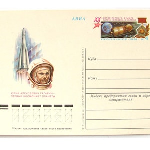 Può includere: Cartolina vintage con un razzo in partenza, un ritratto di Yuri Gagarin in tuta spaziale e una rappresentazione di un'astronave. Il testo include "Yuri Gagarin - Primo cosmonauta del pianeta".