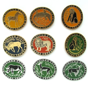 以下が含まれることがあります： 黒と白の動物のイラストが描かれた、丸い金色のピンが9つ。各ピンには、ロシア語で「MOSKOVSKIY ZOOPARK」と「FAUNA AFRIKI」の文字が書かれている。描かれている動物は、シマウマ、ライオン、サイ、ガゼル、サル、ヌー、センザンコウなどです。