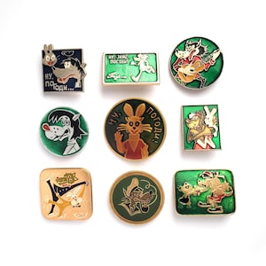 May include: A collection of nine metal enamel pins featuring characters from the cartoon Nu, Pogodi!. The pins are round, square, and rectangular, displaying various scenes with a wolf and a hare in green, gold, black, and red colors.