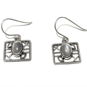 May include: Silver dangle earrings with a square frame and a gray oval gemstone. The frame has a delicate design with a criss-cross pattern and small leaf accents.