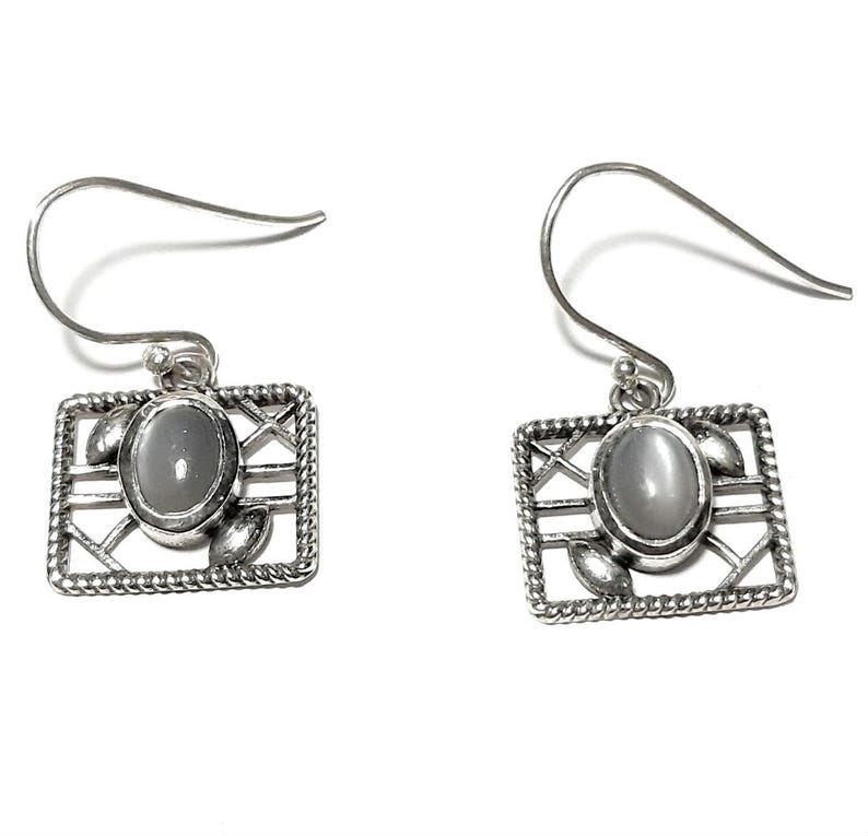 May include: Silver dangle earrings with a square frame and a gray oval gemstone. The frame has a delicate design with a criss-cross pattern and small leaf accents.