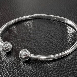 Op de afbeelding: Een zilveren armband met twee ronde, gladde uiteinden. De armband is open en heeft een eenvoudig, minimalistisch ontwerp.
